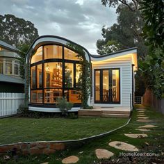 a modern house with an oval shaped roof and glass walls on the outside, surrounded by greenery