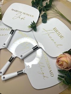 three white paddles with gold writing on them next to some flowers and greenery