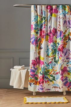 a shower curtain with colorful flowers on it next to a towel rack and toilet paper