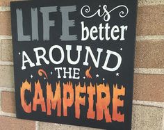 a sign that says life is better around the campfire on a brick wall next to a fire hydrant