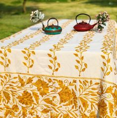 two tea kettles sitting on top of a table covered in yellow and white cloth