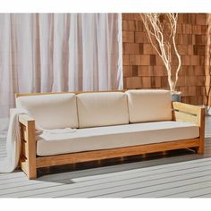 a white couch sitting on top of a wooden floor next to a plant in a vase