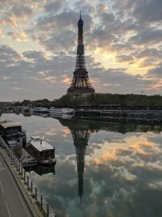 the eiffel tower is reflected in the water at sunset, with boats on the river below