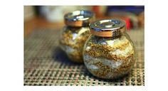 two glass jars filled with different types of spices on top of a cloth covered table