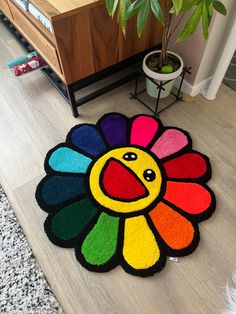 a multicolored rug with a smiley face on the floor next to a potted plant