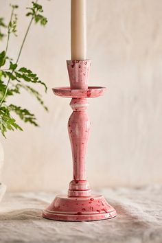 a pink candle holder sitting next to a potted plant on a tablecloth covered surface