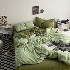 an unmade bed with green sheets and checkered flooring in a white walled room