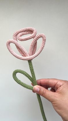 a hand holding a pink crocheted flower on a green string with the letter o