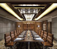 an empty conference room with brown leather chairs and long tables in front of a chandelier