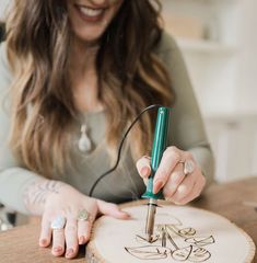 a woman is working on a wood carving with a green pen and some ink in her hands