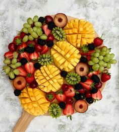 a large platter of fruit is arranged on a marble surface with a wooden spatula