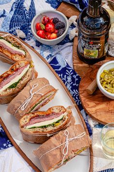 several sandwiches are sitting on a platter next to bowls of fruit and condiments