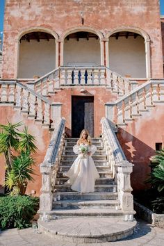 a woman in a wedding dress standing on the steps of a building with stairs leading up to it