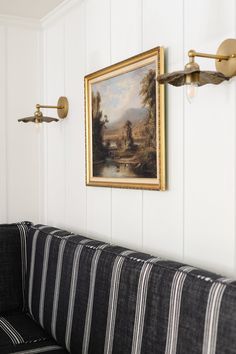 a painting hangs on the wall next to a black and white striped couch in a room