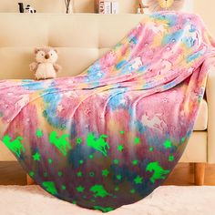 a teddy bear is sitting on a couch under a blanket that has green stars all over it