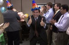 a man in a suit and party hat giving the thumbs up with balloons around him