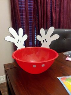 two mickey mouse cutouts are placed in a red bowl on a table next to a window