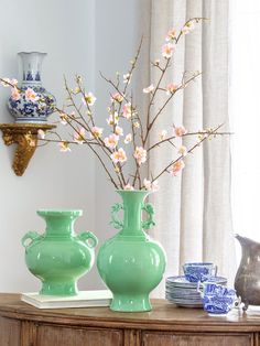 two green vases sitting on top of a table next to each other with flowers in them