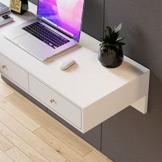 a laptop computer sitting on top of a white desk next to a potted plant