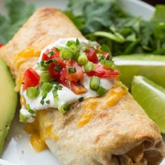 a white plate topped with a burrito next to a salad and avocado