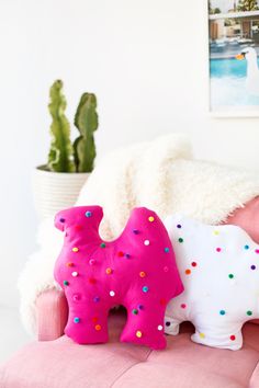 a pink elephant toy sitting on top of a pink couch next to a potted cactus