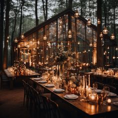 a long table with candles and flowers in front of a large glass building surrounded by trees