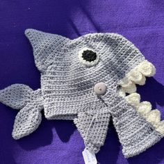 a crocheted hat with a fish on the front and side, sitting on a purple surface