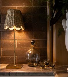 a table with a lamp, vase and two glasses on it next to a brick wall