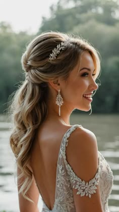 a woman with long hair wearing a wedding dress and earrings on her head is standing near the water