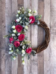 a wreath with red roses and greenery on a wooden background, ready to be used as a decoration