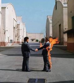 two men in suits shaking hands with fire coming out of the back of their heads