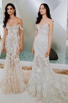 two women in wedding gowns standing next to each other with one woman wearing an off the shoulder dress