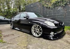 a black sports car parked in front of a wall with ivy growing on it's side