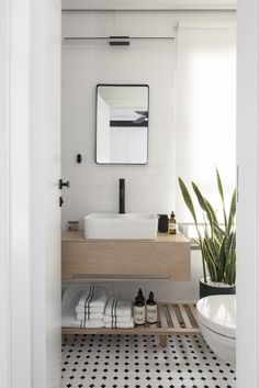 a white bathroom with black and white tile flooring, a wooden sink vanity and mirror