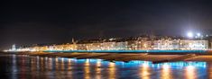 the city is lit up at night with lights reflecting off the water and buildings in the background