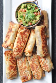 a white plate topped with rolls and guacamole next to a bowl of salsa