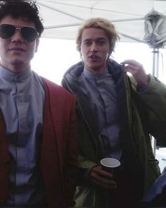 two men standing next to each other in front of a white tent holding coffee cups