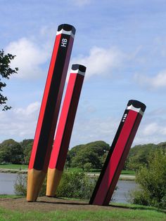 two large red and black pencils are in the grass next to a body of water