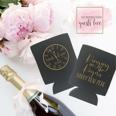 two black and gold wedding favors next to a bottle of wine with pink peonies