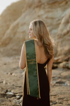 a woman in a black dress is holding a green sash with gold writing on it