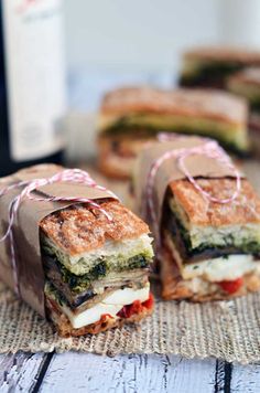 two sandwiches wrapped in brown paper on top of a cloth covered table with red and white twine