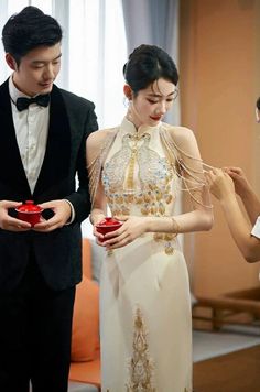 a man and woman standing next to each other in formal wear, holding red boxes