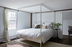 a white bed sitting in a bedroom on top of a wooden floor next to a window