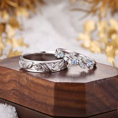 two wedding rings sitting on top of a wooden box in front of some gold leaves