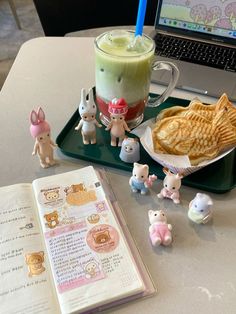 an open book on a table next to small figurines and a cup of drink