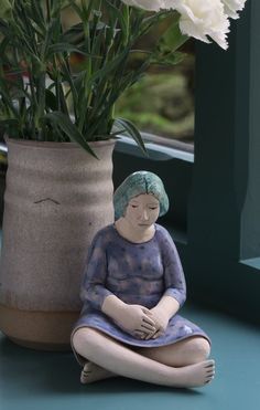 a small statue sitting on the ground next to a vase with white flowers in it