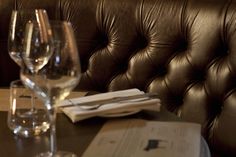 two wine glasses sitting on top of a wooden table next to a menu and napkins