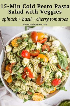 a white bowl filled with pasta salad and topped with spinach, basil, cherry tomatoes and mozzarella