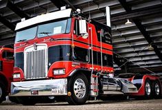 a red and black semi truck parked in front of a large warehouse building with lots of windows