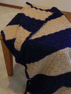 a blue and white crocheted blanket sitting on top of a wooden bench next to a wall